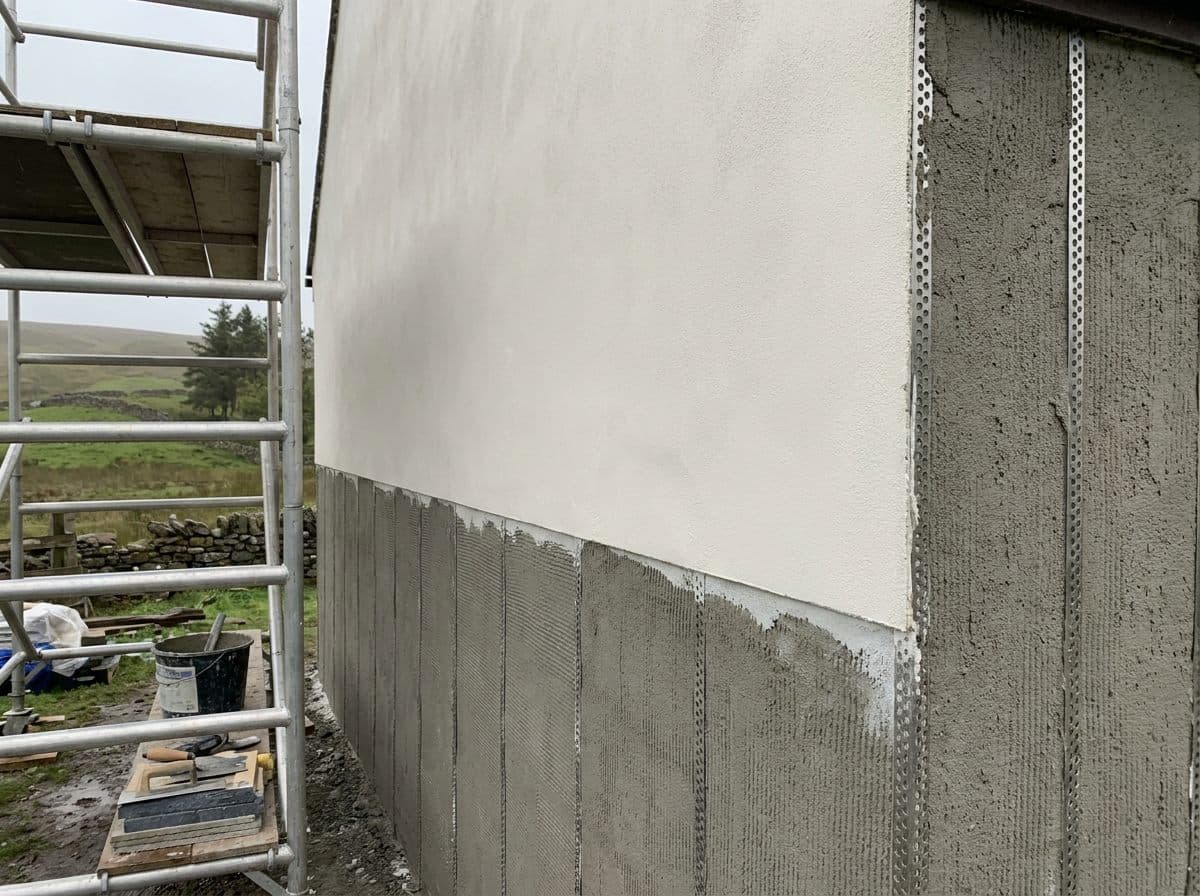 External wall part finished in smooth off-white render over a grey base coat, with scaffolding alongside